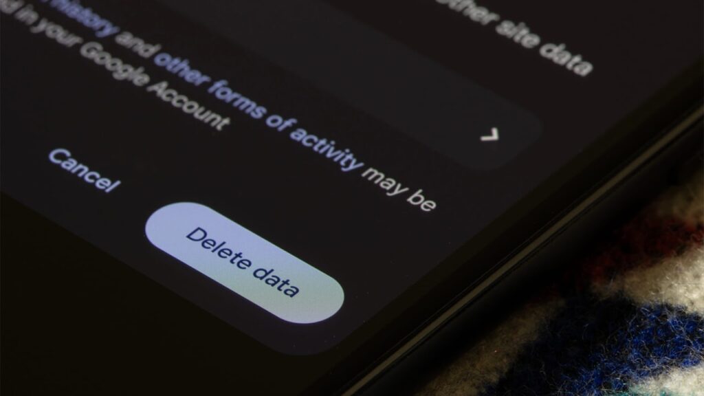Close-up angled view of a smartphone screen in dark mode, highlighting a "Delete data" button within a Google account activity settings menu.
