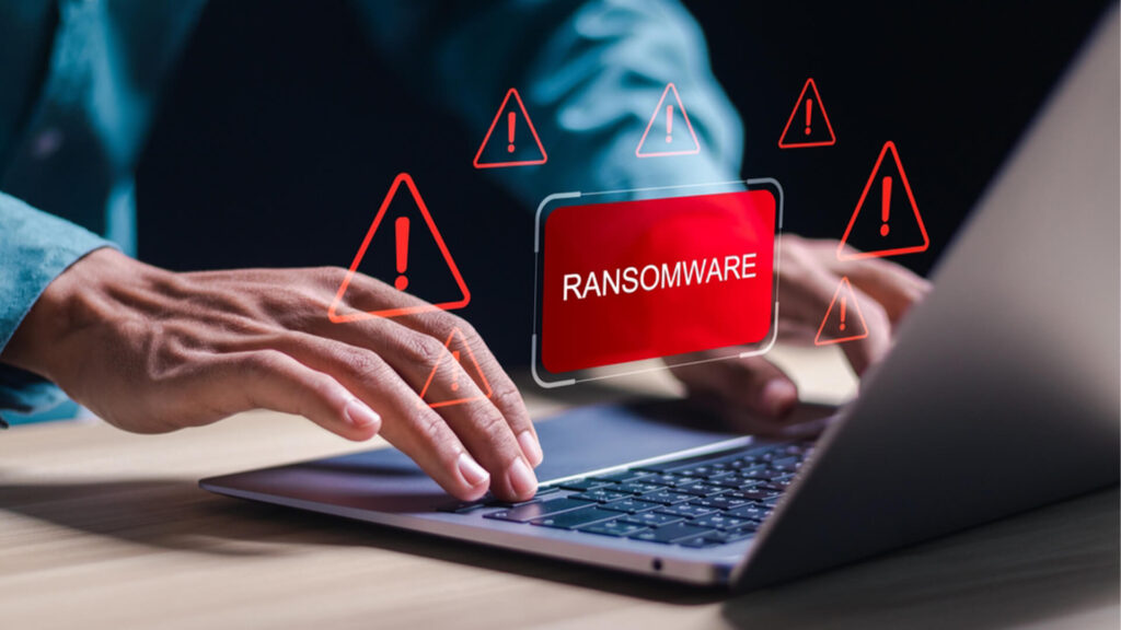 Image of a person using a laptop with ransomware warning alert with red exclamation icons representing cyber threats & data security risks