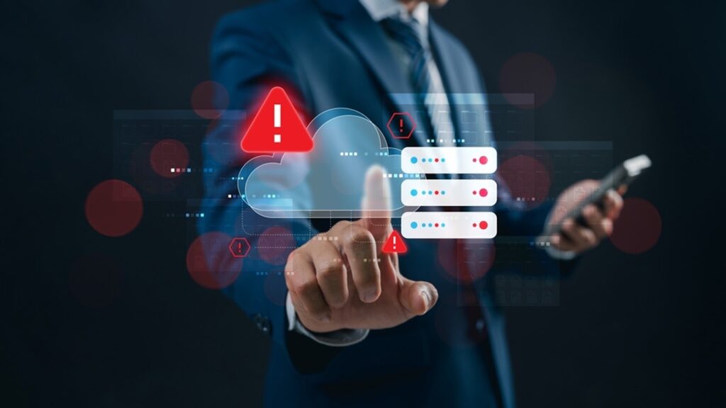 A business professional in a suit pointing to a futuristic digital interface displaying a red warning alert on a cloud server icon, indicating a system error or security risk.
