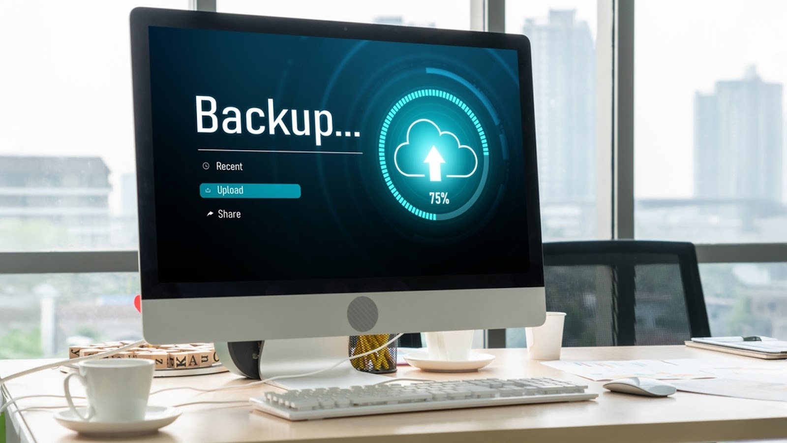 An office desktop computer monitor displaying a data backup progress screen at 75% completion with a cloud upload icon, sitting on a desk next to a coffee cup.