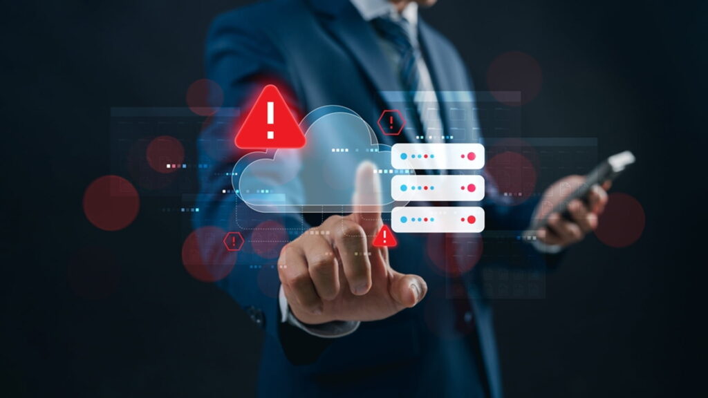 A business professional in a suit pointing to a futuristic digital interface displaying a red warning alert on a cloud server icon, indicating a system error or security risk.